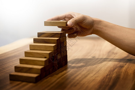 人手把安排堆叠以促进发展的木制块作为阶梯增长概念和成功计划背景图片