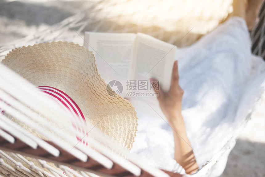 年轻女士在热带沙滩躺在吊床上读书图片