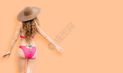 橙色背景下穿泳衣戴遮阳帽的美女背影图片