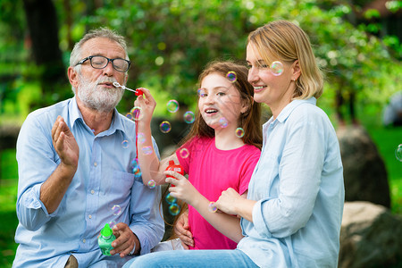 快乐的家庭在暑假周末去花园度假时一起吹着肥皂泡泡图片