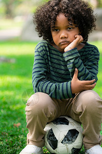 小男孩坐在球场的足球上思考图片