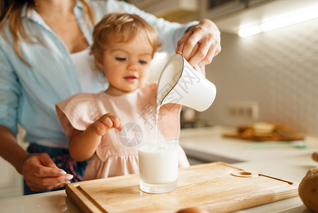 年轻母亲和孩子把牛奶倒进一个杯子做糕点的原料图片