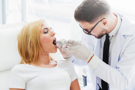 年轻英俊的牙医检查在科诊所坐医椅子上的幸福妇女病人牙齿科护理概念图片