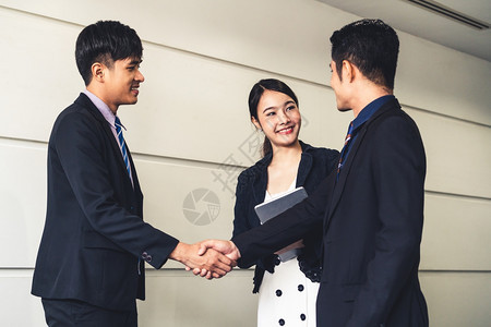 商人在办公室会议与另一名商人握手年轻的亚洲秘书女士站在他们旁边图片