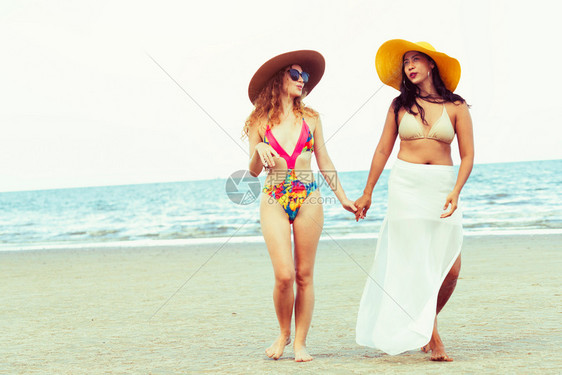 暑假穿着比基尼的快乐女人牵着手行走在热带沙滩上图片