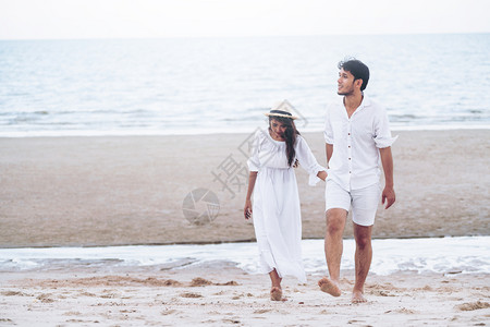 暑假蜜月期快乐的年轻夫妇在海滩上散步图片素材