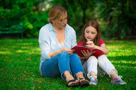 户外公园中母亲和孩子在草坪上看书阅读图片