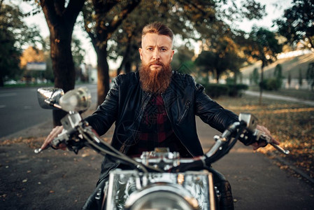 穿着皮夹克的长胡子摩托车手坐在古典直升机前视旧式自行车骑摩托的手图片