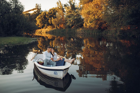 夏日宁静的湖上浪漫夫妇带着水果篮躺在一条船上图片