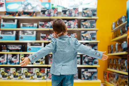 男孩在超市上选玩具在儿童商店的书架上后视图片