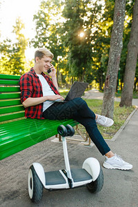 在公园长椅上坐着打电话的年轻男子图片