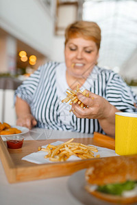在商场餐厅吃高卡路里食品的胖女人在餐桌上吃垃圾晚饭的超重女肥胖问题在商场吃高卡路里食品的胖女人图片