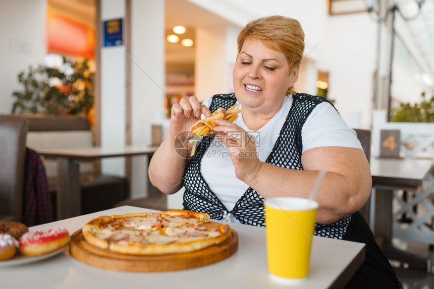 胖女人在快餐厅吃披萨不健康的食物胖女人在餐桌上吃垃圾晚饭肥胖问题女人在快餐厅吃披萨图片