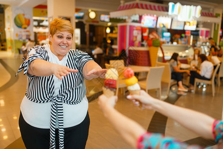 胖女人在快餐商场厅买两块冰淇淋超重女吃冰淇淋肥胖症女人吃冰淇淋快餐店背景图片