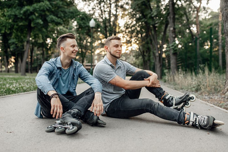 两个男孩穿着轮滑鞋坐在公园的路上图片