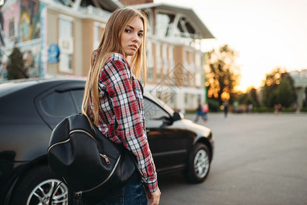 年轻女司机背着黑色包包靠在车旁图片