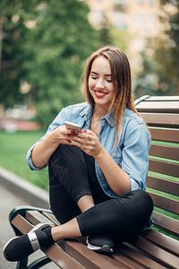 在公园长凳上使用手机的年轻女子图片