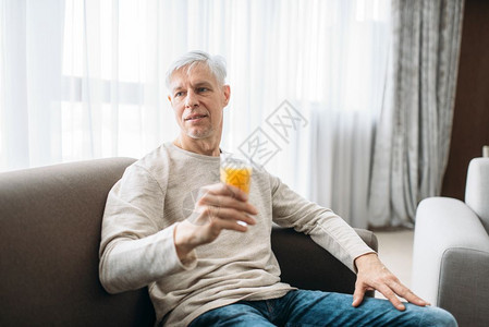 坐在沙发上喝新鲜果汁的快乐成年男子图片