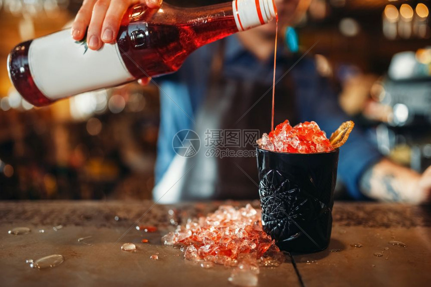 酒吧招待将饮料倒入满冰的黑玻璃杯中图片