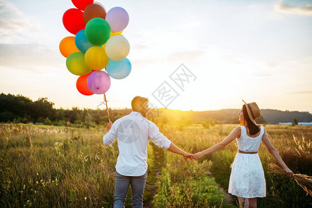 情侣拿着彩色气球在麦田里约会图片
