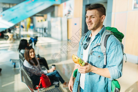 携带背包的男旅游者手拿汉堡在机场等待图片