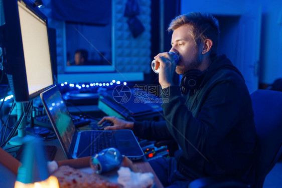 男游戏家在工作场所用笔记本电脑和台式笔记本电脑和台式笔记本喝能量饮料玩游戏夜间生活方式图片