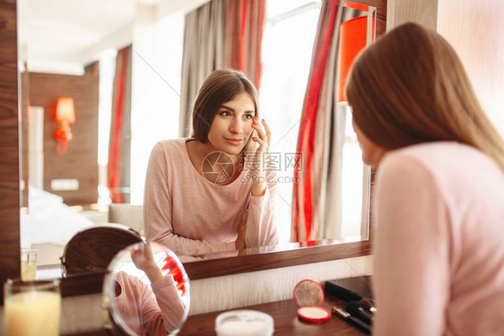 在卧室镜子前的女青年穿着睡衣照镜子做早晨的面部清洗程序图片