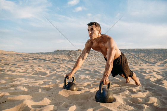 沙漠上双手握着壶铃做俯卧撑的肌肉男图片