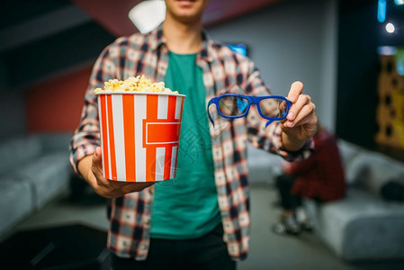 影院大厅的男观众在表演前的电影厅里展示戴3D眼镜和爆米花图片