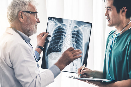 高级男医生在院与另一名生务人员和生一起工作时检查病人胸部受伤的x光片图片