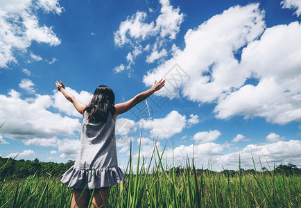 青草地上的年轻美女在夏日向阳光晴朗的蓝天伸出双臂逃跑和冥想的概念图片