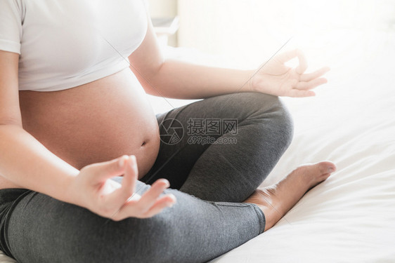 怀孕妇女在家里卧室的床上做瑜伽锻炼图片