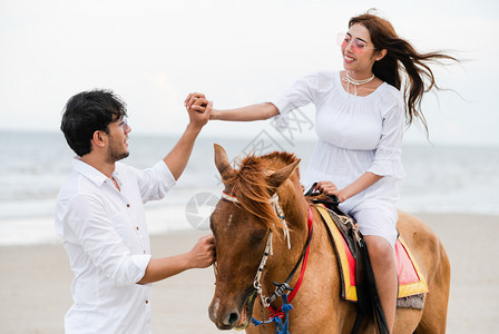 年轻夫妇在暑假海滩骑着马图片