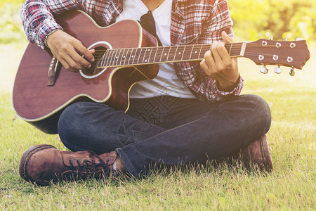 男人和手弹吉他坐在绿色草地上自然背景音乐吉他和自然乡村民歌来自音响吉他男人拿着吉他图片