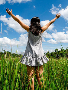 青草地上的年轻美女在夏日向阳光明媚的蓝天伸展手臂图片