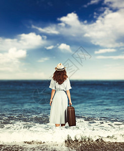 带着行李的年轻女子沿着海洋的岸行走图片