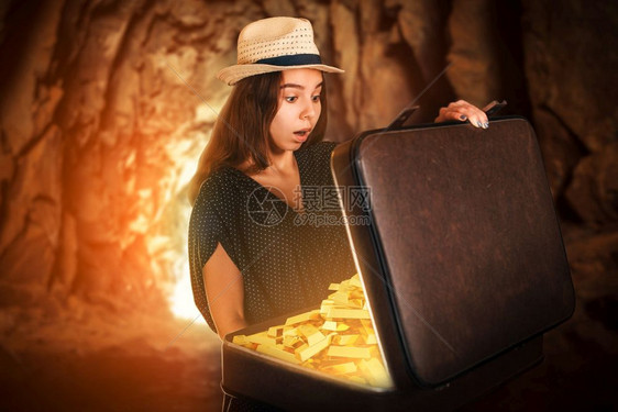 年轻女人站在洞穴里拿着一个半开放的手提箱装满金条古董风格冒险概念图片