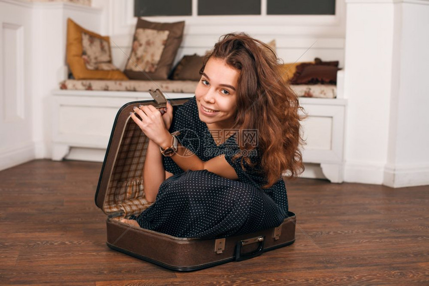 年轻女子试图爬上手提箱旧式旅行概念图片