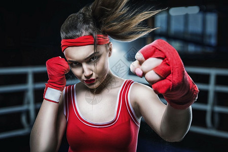 女拳击手戴着红手套穿着运动服在健身房训练拳击图片