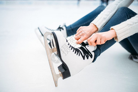 冬天年轻人穿着溜冰鞋在户外滑冰绑鞋带高清图片