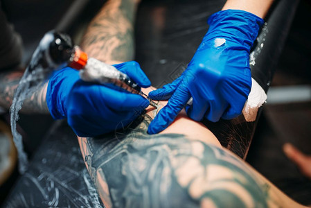 女纹身师用机器在男肩上做纹身在沙龙专业纹身师用机器在男肩上做纹身图片