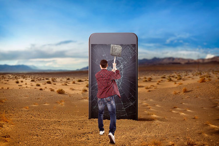 男人用大智能手机屏幕砸碎了一把锤子沙漠谷在背景上操纵意识缩放效果图片