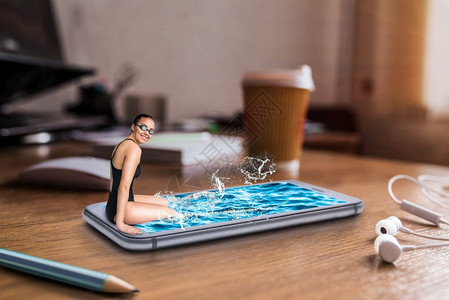 女游泳者坐在大型有水的电话屏幕边缘坐在有大咖啡杯的桌边有移动和通信技术者社会图片