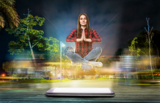 瑜伽中的年轻女子在晚间街上大电话悬浮面装有荧光屏幕对背景有长期光效应图片