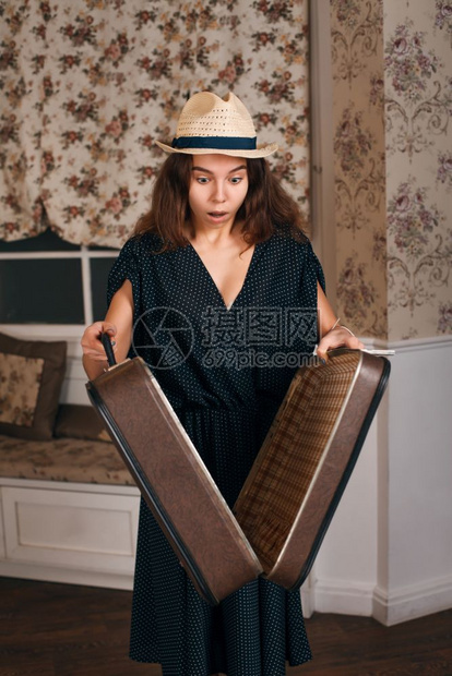 身着黑衣的年轻女子手里拿着半开放的手提箱古老风格沙发和窗帘的图片
