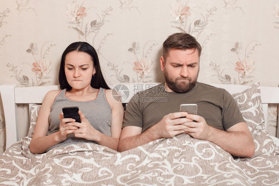 年轻夫妇在床上看手机图片