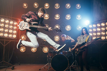 吉他手在拜斯上演奏跳跃时的快照背景有灯光的舞台摇滚乐队音会图片