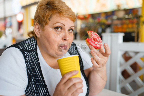 肥胖症超重的女人吃甜甜圈图片