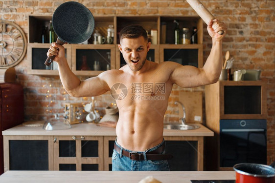 赤身裸体的男性子拿着煎锅,在厨房上打滚针。 裸体男性子在家准备早餐,不穿衣服准备食物。图片