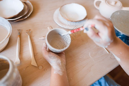 女陶工用毛笔画一壶陶艺作坊塑造碗的女人手工陶瓷艺术粘土餐具女陶工用毛笔画壶陶器图片